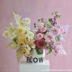 a vase filled with lots of flowers on top of a white table next to a pink wall