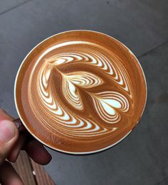 a person holding up a cup of coffee with swirl designs on it's foamy surface