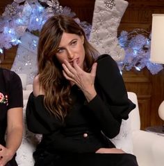 two women sitting on a white couch in front of christmas decorations, one holding her hand to her mouth