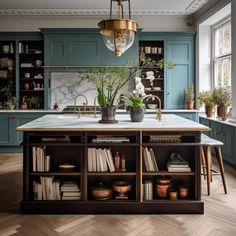 a kitchen with blue cabinets and marble counter tops, an island in the middle is surrounded by potted plants