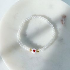 a white beaded bracelet with a heart charm on it sitting on a marble surface