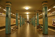 an empty subway station with people sitting on benches in the hallway and posters on the walls