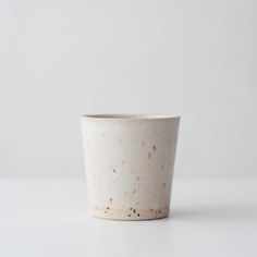 a white cup with speckles on it sitting on a table next to a wall