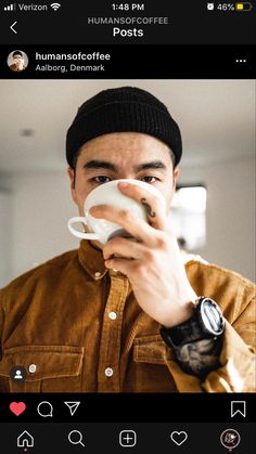 a man drinking from a coffee cup while wearing a beanie on top of his head