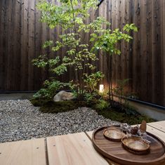 a wooden table sitting on top of a gravel covered ground next to a small tree