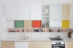 a kitchen with white cabinets and multicolored cupboards on the wall above the sink