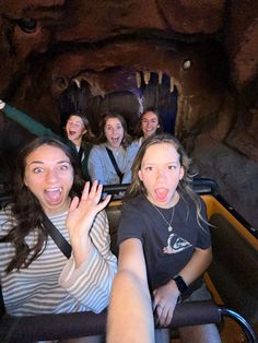 four girls are riding on a roller coaster at the amusement park and making funny faces