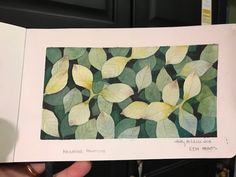 a person holding up an open book with watercolors on it and green leaves