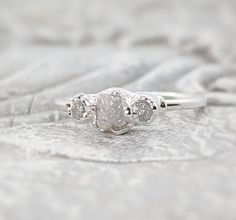 a three stone diamond ring sitting on top of a piece of cloth