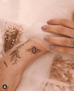 a woman's hand with a bee tattoo on her left arm, and flowers in the background