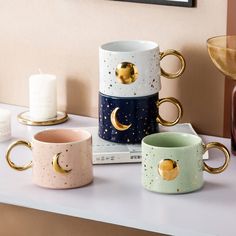 three coffee mugs sitting on top of a table next to candles and other items