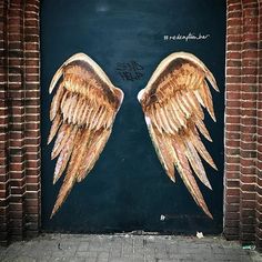 two large wings painted on the side of a brick wall next to a doorway with graffiti