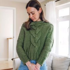 a woman standing in front of a couch with her hands on her hips wearing a green sweater