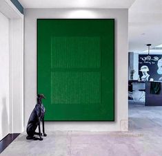 a black dog sitting in front of a large green screen on the wall behind it