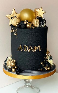 a black and gold birthday cake with stars on top that says adam in gold lettering