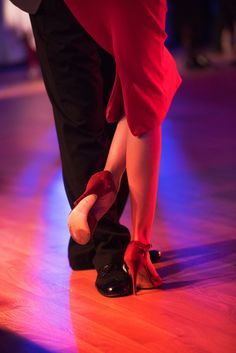 the legs and feet of two people in red shoes on a dance floor with lights behind them