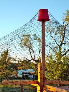 a red bucket sitting on top of a wooden post in front of a wire fence