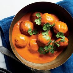 a metal bowl filled with meatballs covered in sauce and garnished with cilantro