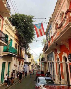 people are walking down the street in front of colorful buildings with flags hanging above them