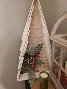 a christmas tree made out of sheet music is on a shelf next to a candle