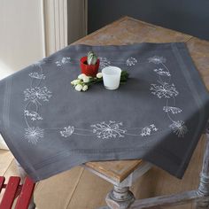 a table topped with a gray table cloth covered in white flowers and a candle on top of it