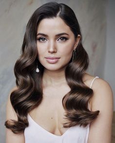 a woman with long brown hair is posing for the camera, wearing earrings and a white dress