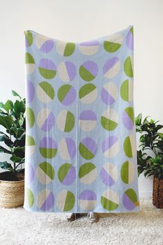 a blue blanket with green and purple leaves on it sitting next to potted plants