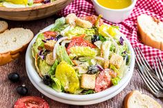 a close up of a salad in a bowl on a table with bread and olives