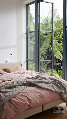 a bed sitting in front of a large window next to a plant filled room with lots of windows