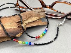 Tiny black seed beads necklace with chakra colors gemstones. Elegant and bohemian eye glasses necklace chain in black tones with rainbow touches in the seven colors of the chakras. The necklace is made with Preciosa Czech seed beads and tiny Amethyst, Turquoise, Jade, Agate, Citrine, Carnelian and Ruby gemstones. Paired with tiny silver plated crystal seed beads, this handmade eyeglass chain will definitely create a unique look. This eyeglass lanyard is made on strong quality beading wire with s Black Glass Beaded Necklaces With Colorful Beads, Black Glass Beaded Necklace With Colorful Beads, Black Glass Beaded Necklaces With Beaded Chain, Black Glass Beaded Necklace With Beaded Chain, Black Spiritual Necklace For Beach, Black Glass Beaded Necklace, Black Bohemian Glass Jewelry, Bohemian Black Glass Jewelry, Black Glass Bohemian Jewelry