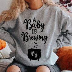 a woman sitting on a bed wearing a sweatshirt that says, a baby is brewing