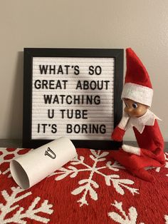 an elf sitting on top of a red blanket next to a sign that says what's so great about watching u tube it's boring