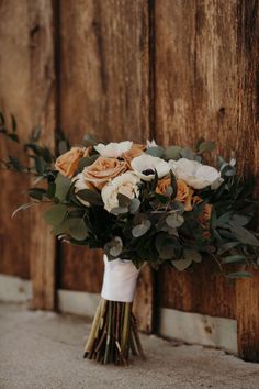 a bridal bouquet is sitting on the ground by a wooden door with greenery