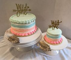 two cakes decorated with gold and pink frosting sitting on top of a cake plate