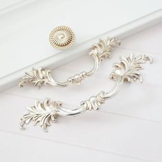 a close up of a drawer handle on a white surface with an ornate design in the middle