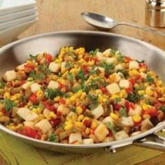 a pan filled with corn and potatoes on top of a wooden table next to silverware