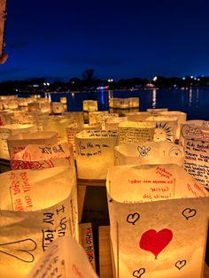 many paper bags with writing on them are lit up at night by the water's edge