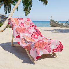 a beach chair on the sand with a pink and white flowered cover over it