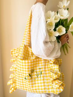 a woman holding a yellow and white bag with flowers in it's back pocket