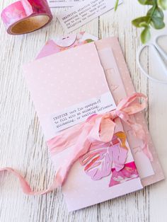 some pink papers with ribbons on top of them next to a pair of scissors and tape