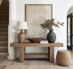 a wooden table with two vases and a lamp on it in front of a staircase