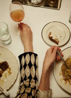 a person sitting at a table with food and drinks in front of them, while holding a knife and fork