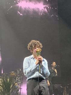 a man standing on stage holding a flower in front of his face with other people behind him