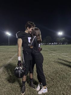 two people standing in the middle of a field at night with their arms around each other