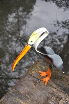 a plastic bird sitting on top of a piece of wood next to the water's edge