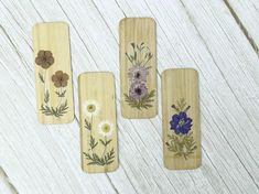 four wooden bookmarks with flowers painted on them sitting on a white wood table next to each other