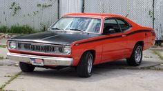 an orange and black muscle car parked in front of a fenced in area with grass