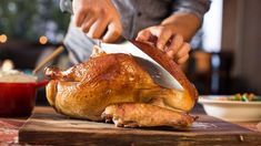 a person cutting up a turkey on top of a wooden cutting board with a knife