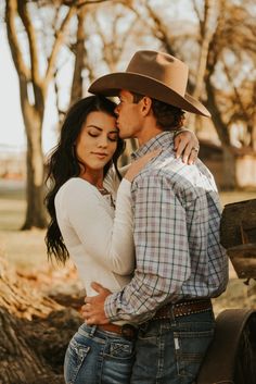 a man in a cowboy hat kissing a woman on the cheek while standing next to a tree