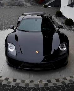 a black sports car parked in front of a white and gray house with cobblestone flooring